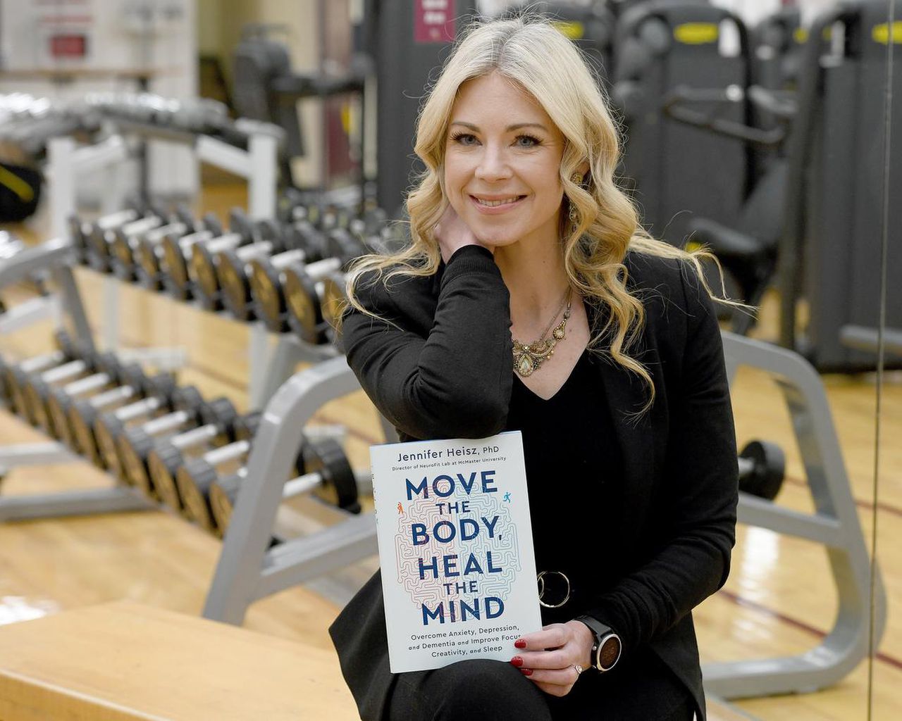 Dr. Jennifer Heisz with book in front of gym equipment